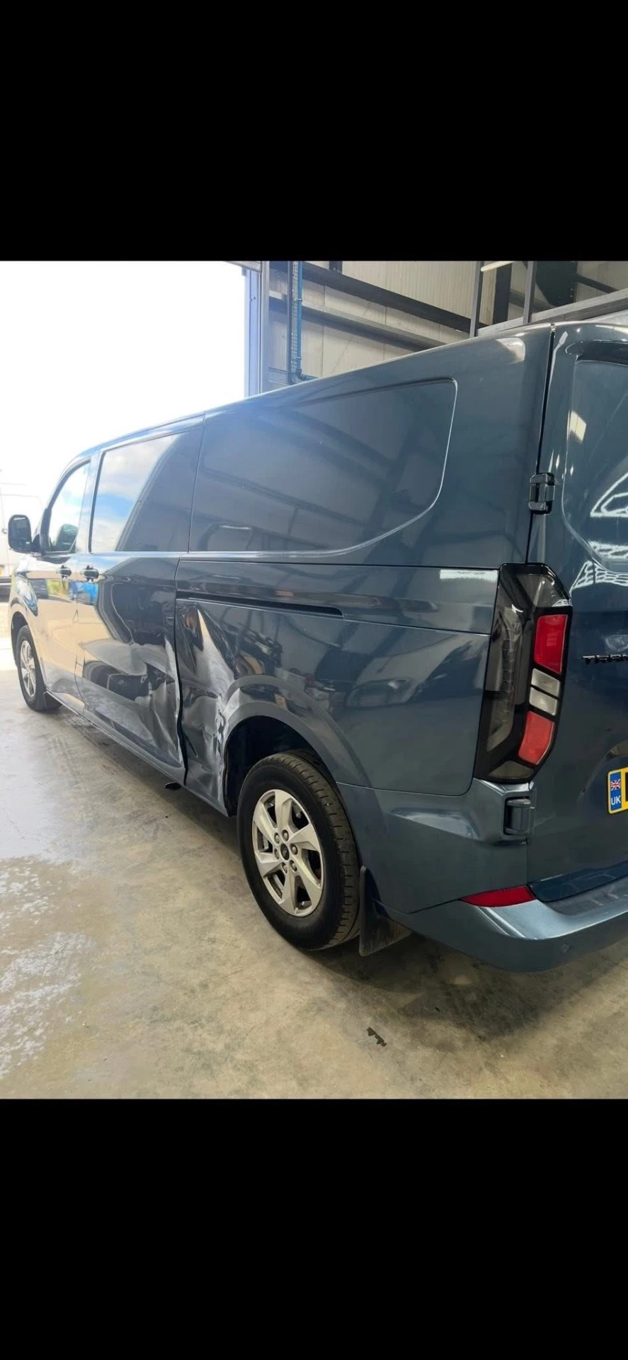 Ford Transit Custom passenger-side accident damage, rear three-quarter view in the workshop