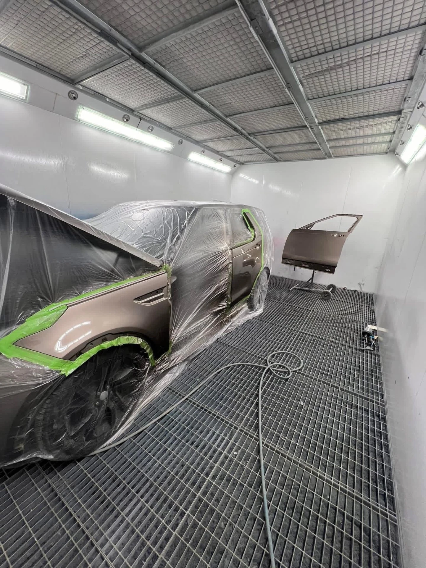 Land Rover Discovery masked in the spray booth with replacement front door on a stand