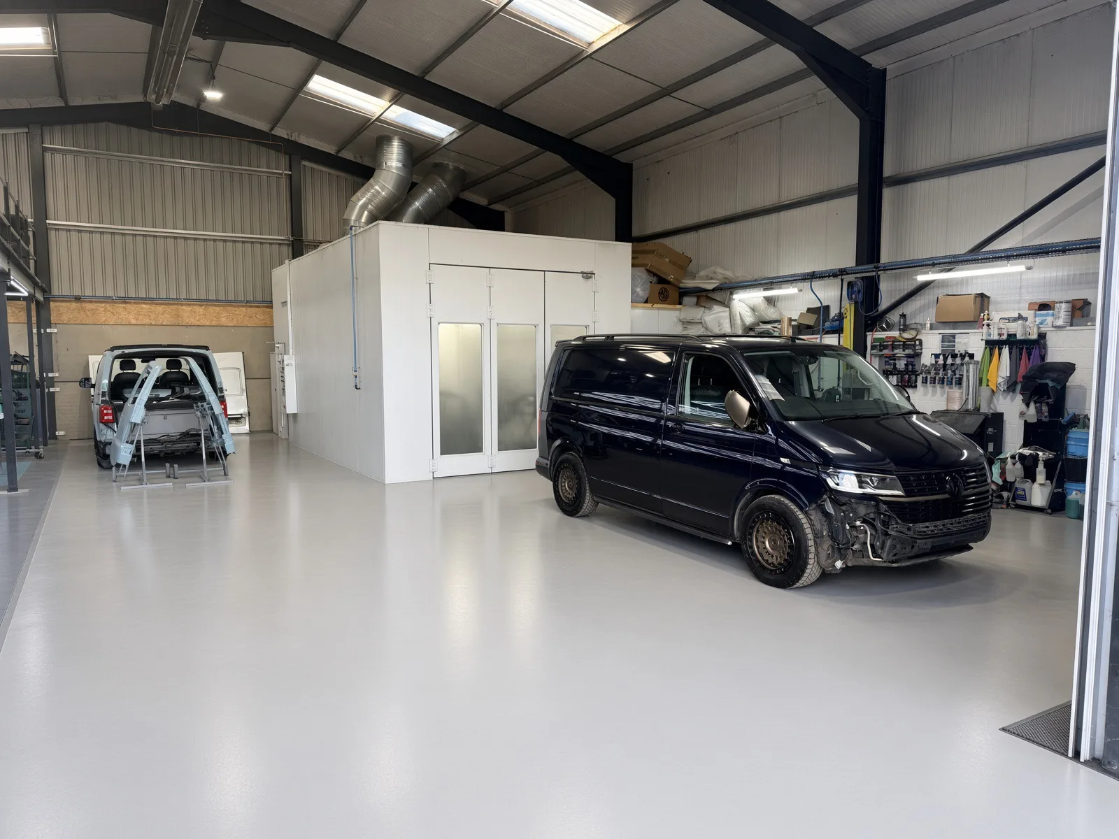 Workshop floor with vans awaiting bodywork beside the enclosed paint booth