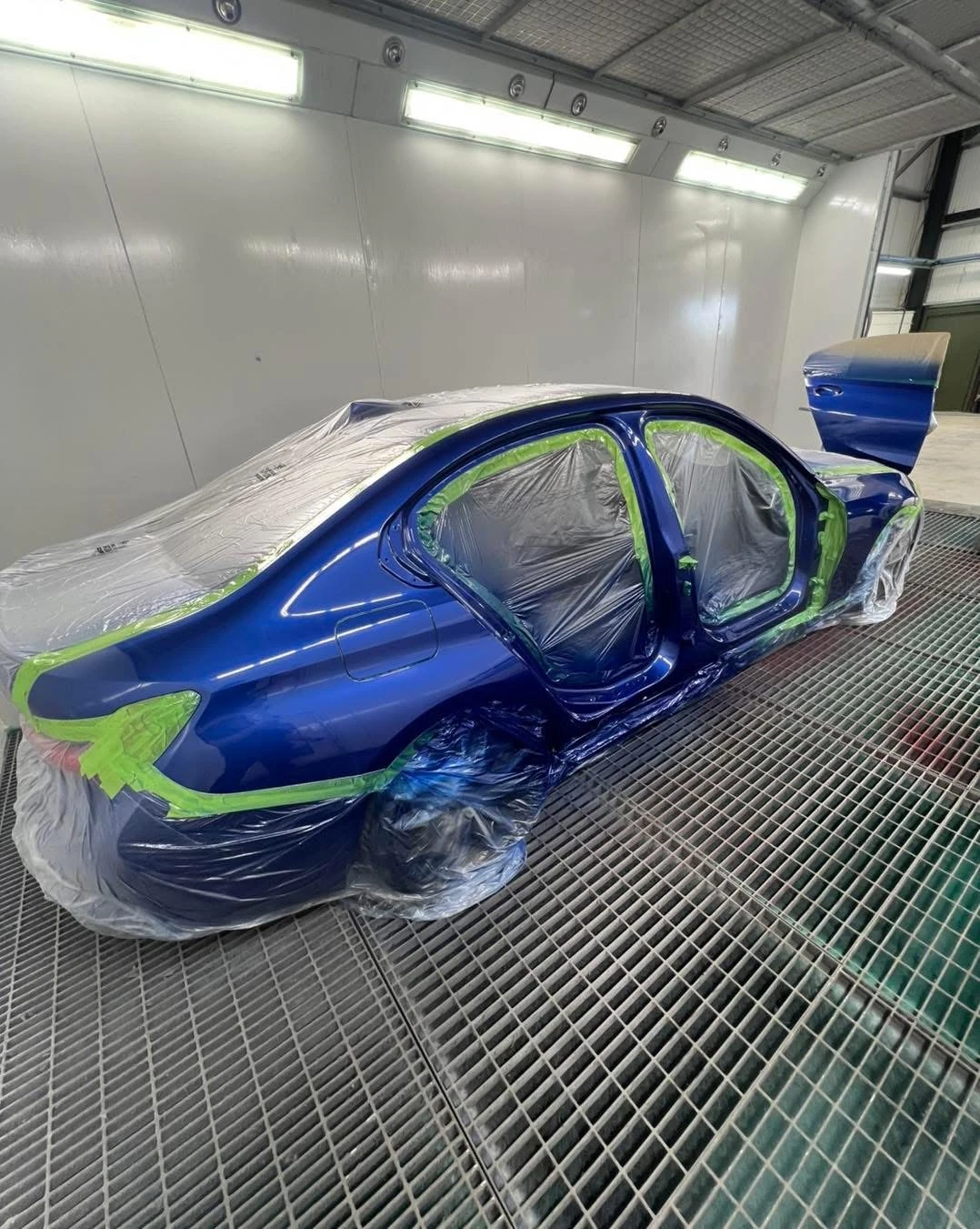 BMW 330i freshly painted blue rear quarter and door openings in the spray booth