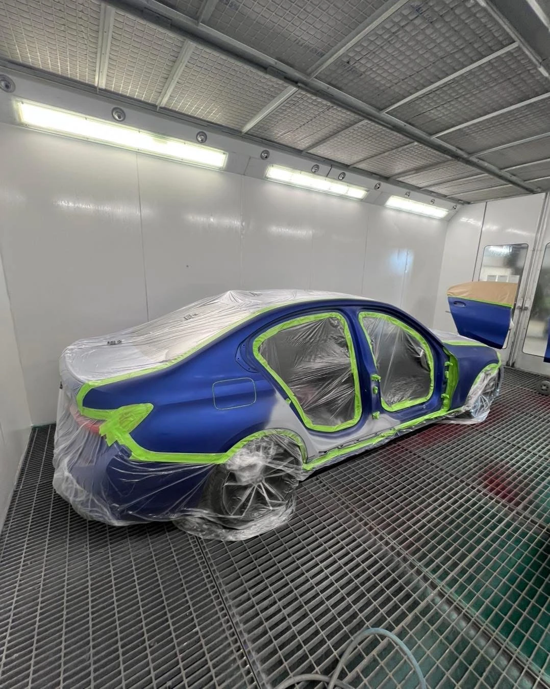 BMW 330i masked in the spray booth with doors removed and rear quarter prepared
