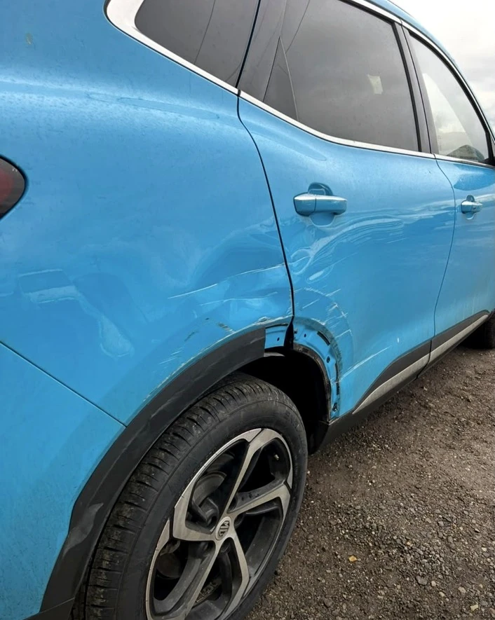 Blue SUV before repair, with a dent to the rear door and wheel arch